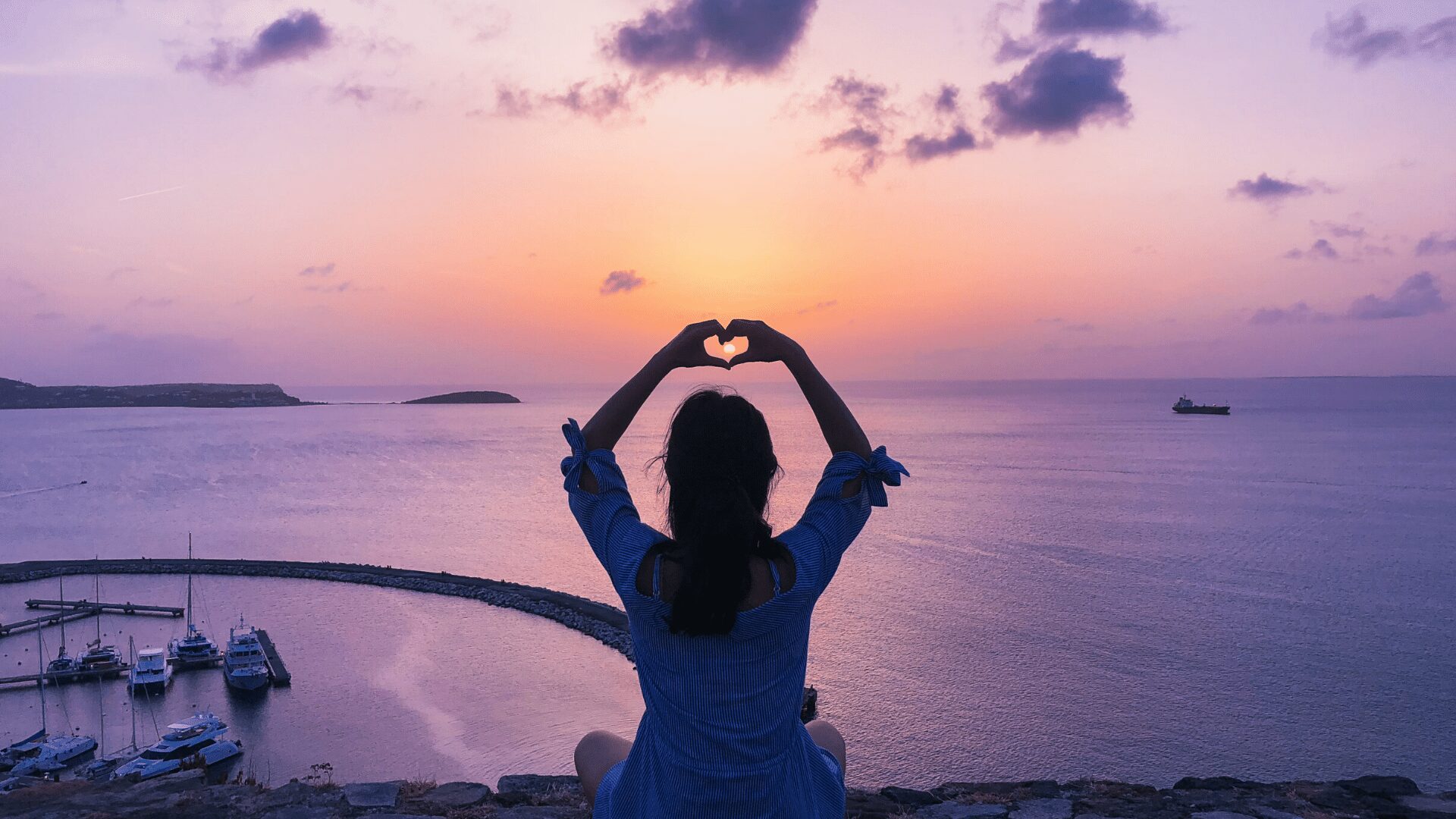 femme de dos devant mer coucher de soleil mauve forme coeur avec ses mains