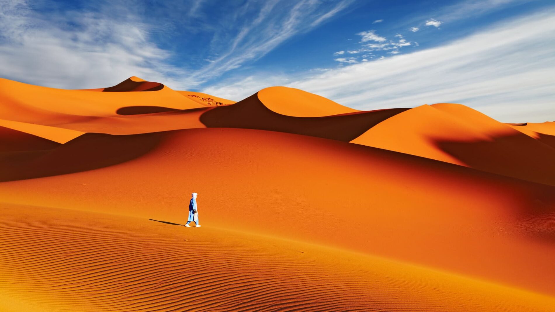 une personne seule marche dans les dunes oranges du désert de sahara
